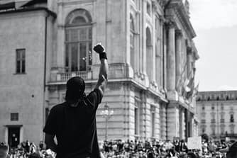 man in black t shirt standing infront of a crowd in protest / manifestation